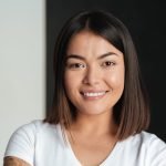 Picture of smiling young asian woman isolated over grey and black wall. Looking at camera.